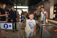 Mały chłopiec jako jeden z pierwszych zwiedzających przechodzi przez bramki prowadzące na wystawę interaktywną. w tle czekają już kolejni stojący w kolejce ludzie.