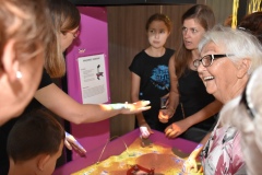 Odwiedzający korzystający z eksponatu "Krajobraz zamkowy" w którym wysokość piasku wpływa na jego kolor, jak w mapie hipsometrycznej.