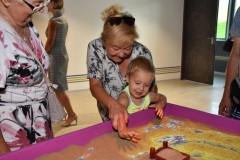 Babcia wraz z wnuczkiem bawią się w piaskownicy eksponatu "Krajobraz zamkowy"